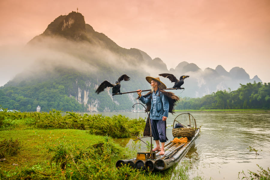Pescador de cormorán en el río frente a un atardecer con montañas